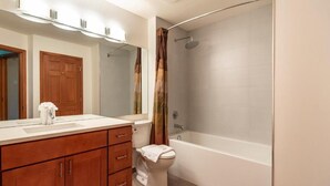 Ein modernes Badezimmer mit einem Holzlagerfläschchen, einer Toilette, einer Badewanne und einer Duschkabine mit Vorhang.