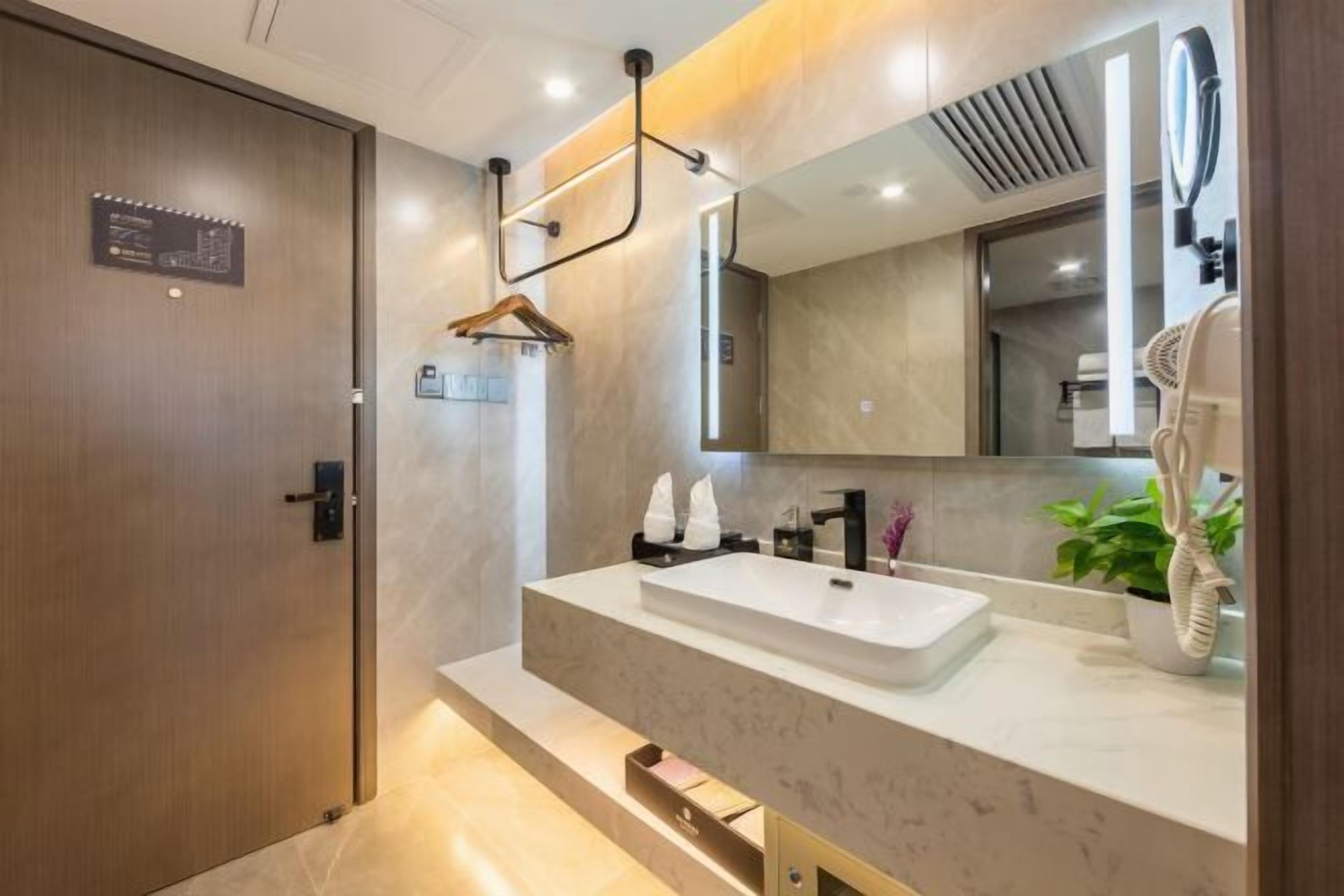 A modern bathroom with a large mirror, a white sink, and a hairdryer on the counter.