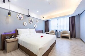 Ein modernes Hotelzimmer mit einem großen Bett, Nachttischen, einem kleinen runden Tisch und einem Sessel.