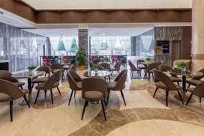 A modern hotel lobby with round tables and chairs, a central plant, and a view through large windows. - Movie Hotel (Guangzhou Pazhou Exhibition Center Store) (Guangzhou)