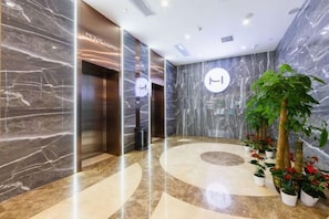 A lobby with marble walls, a reception desk, and potted plants. - Movie Hotel (Guangzhou Pazhou Exhibition Center Store) (Guangzhou)