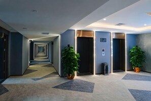 A hotel corridor with a carpeted floor, two potted plants, and a series of doors leading to rooms. - Movie Hotel (Guangzhou Pazhou Exhibition Center Store) (Guangzhou)