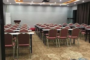 A conference room with rows of tables and chairs, carpeted flooring, and a plain wall. - Movie Hotel (Guangzhou Pazhou Exhibition Center Store) (Guangzhou)