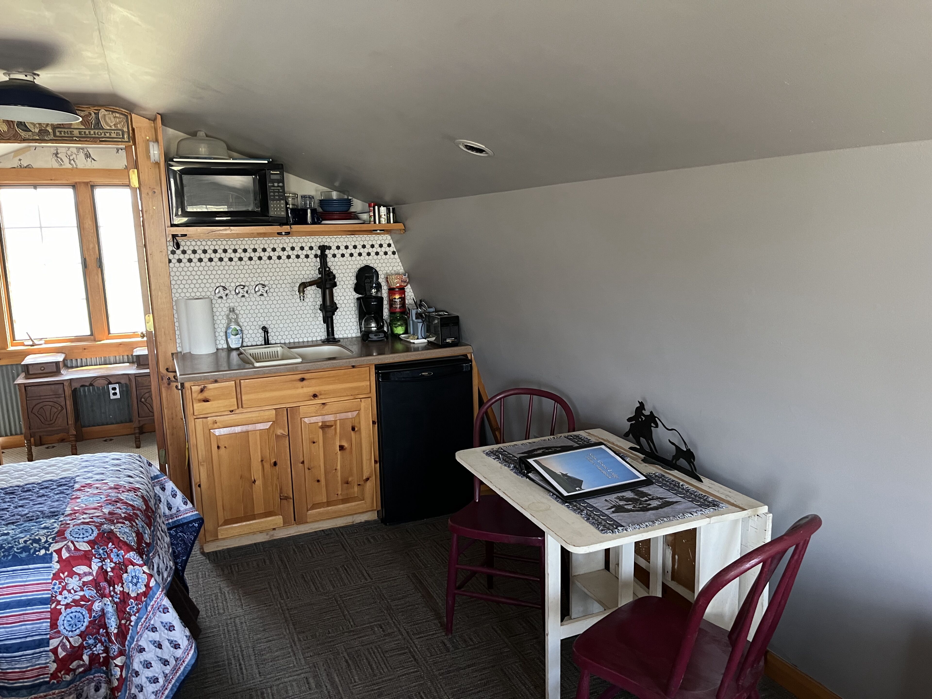 A compact kitchen with wooden cabinets, a microwave, a sink, and a small dining area with a table and chairs.