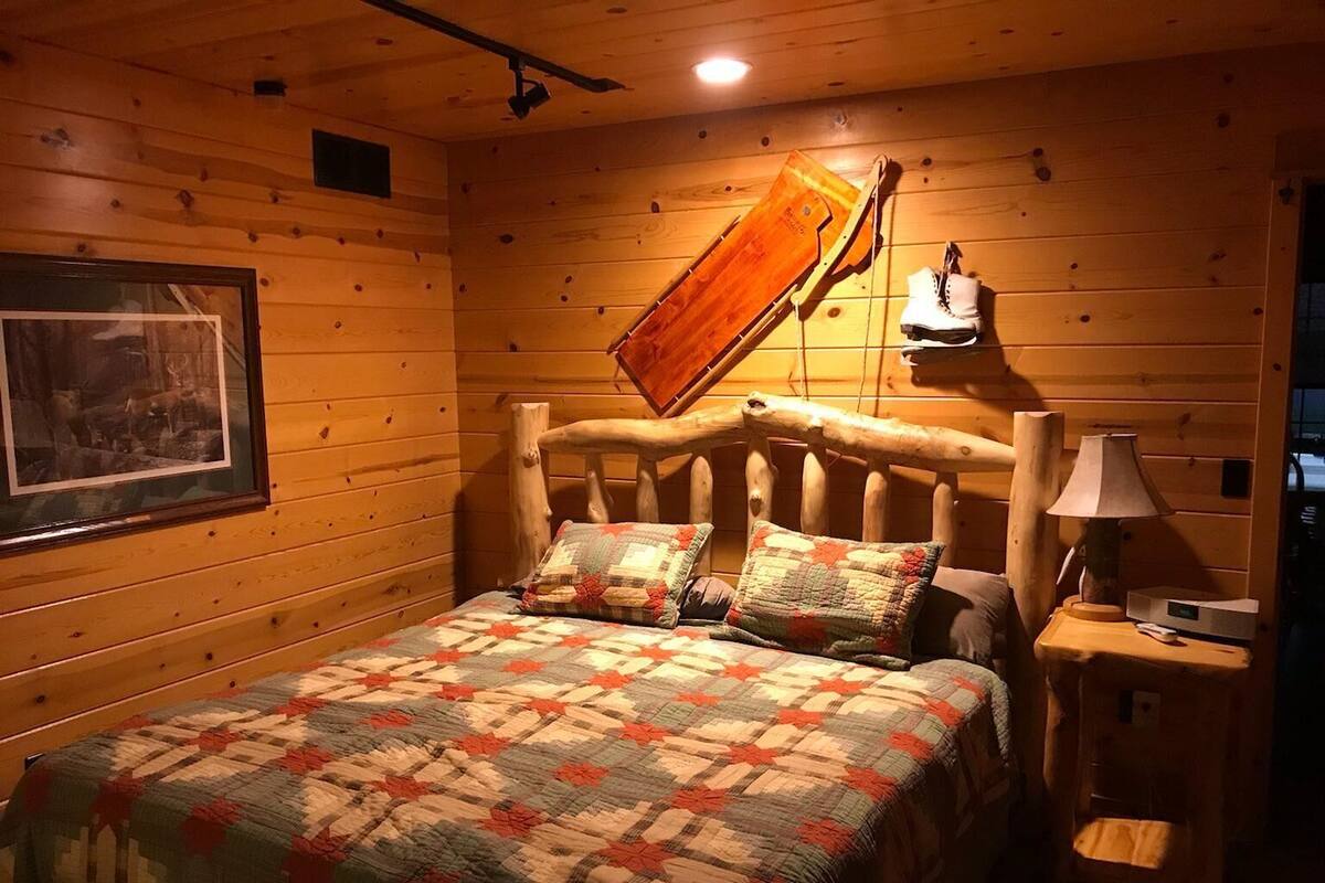 A cozy wooden cabin room with a bed, a framed picture on the wall, and a wooden headboard.