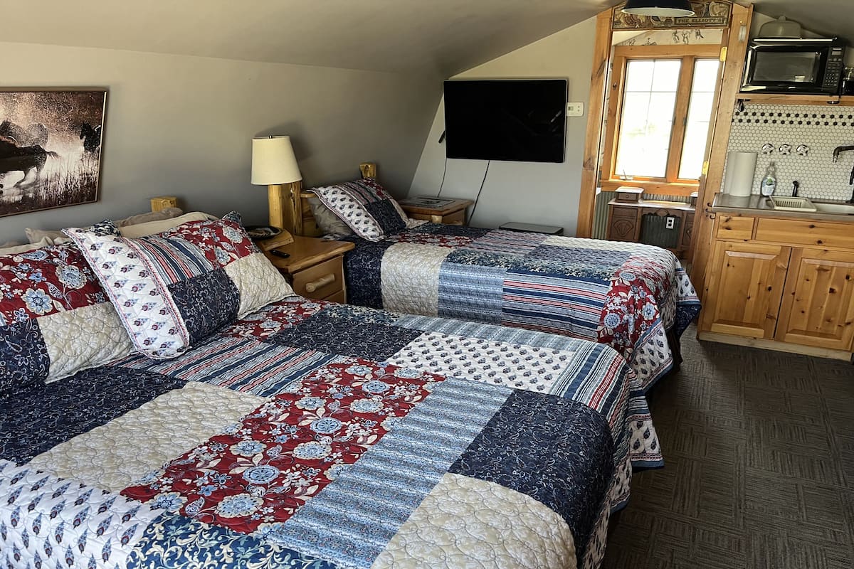 A bedroom with two beds, a wooden cabinet, a microwave, and a painting on the wall.