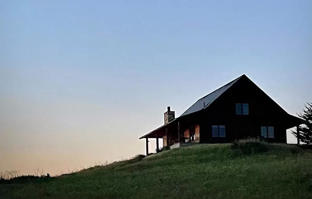 Een huis met een schuin dak, schoorsteen en veranda.