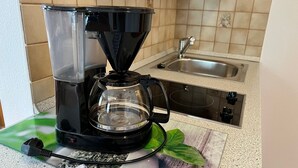 A coffee maker on a kitchen counter with a sink and a tiled backsplash.