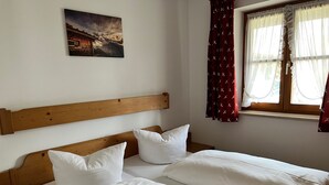 A room with a wooden headboard, two single beds with white linens, a painting on the wall, and a window with sheer curtains.