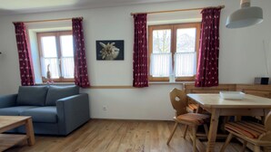 A living room with a sofa, dining table, chairs, and windows with curtains.