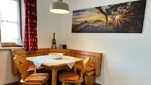 A corner dining area with a wooden table and bench, a checkered tablecloth, and a painting of a mountain landscape on the wall.