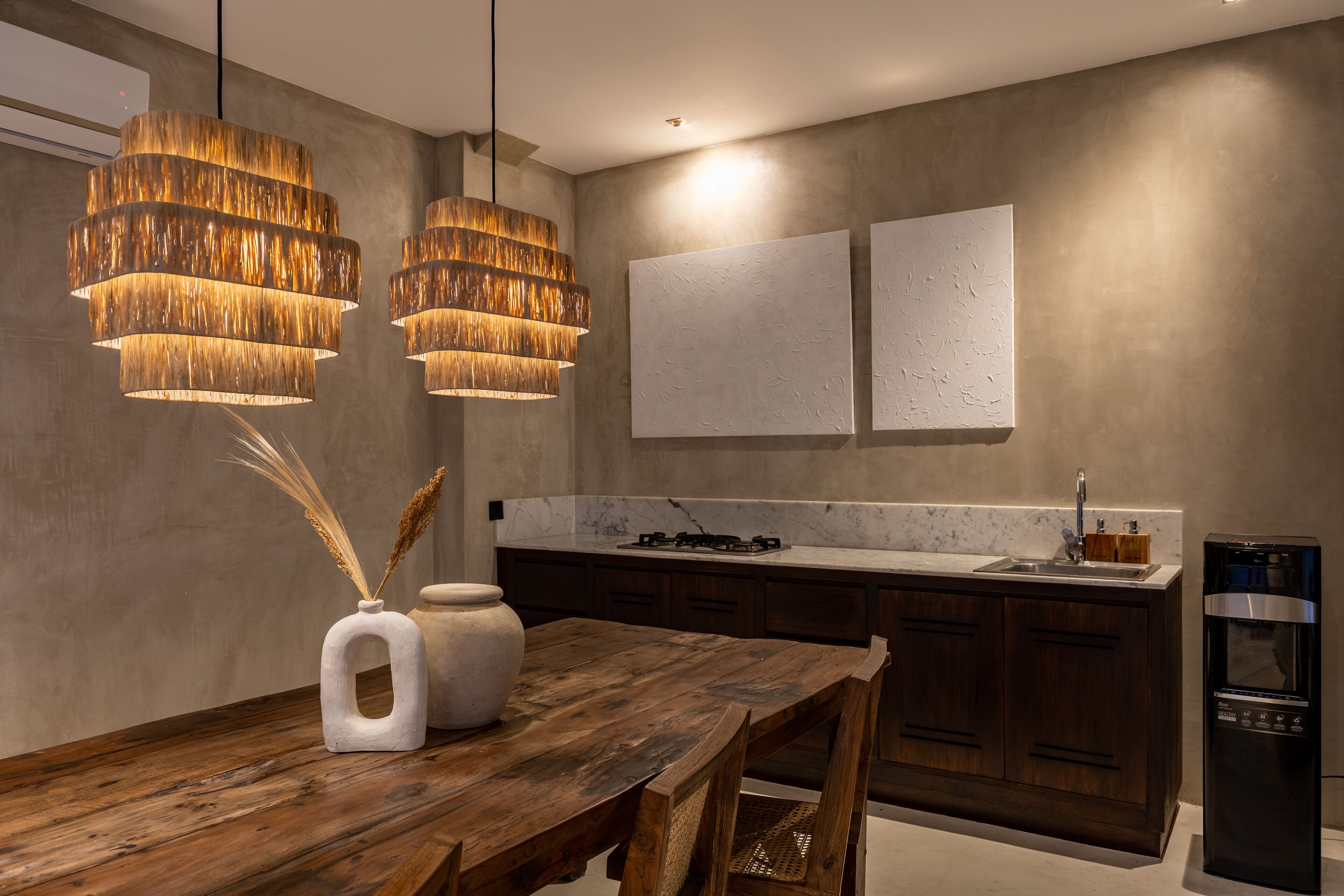 A modern kitchen with a wooden dining table, two pendant lights, a built-in oven, and a marble countertop.