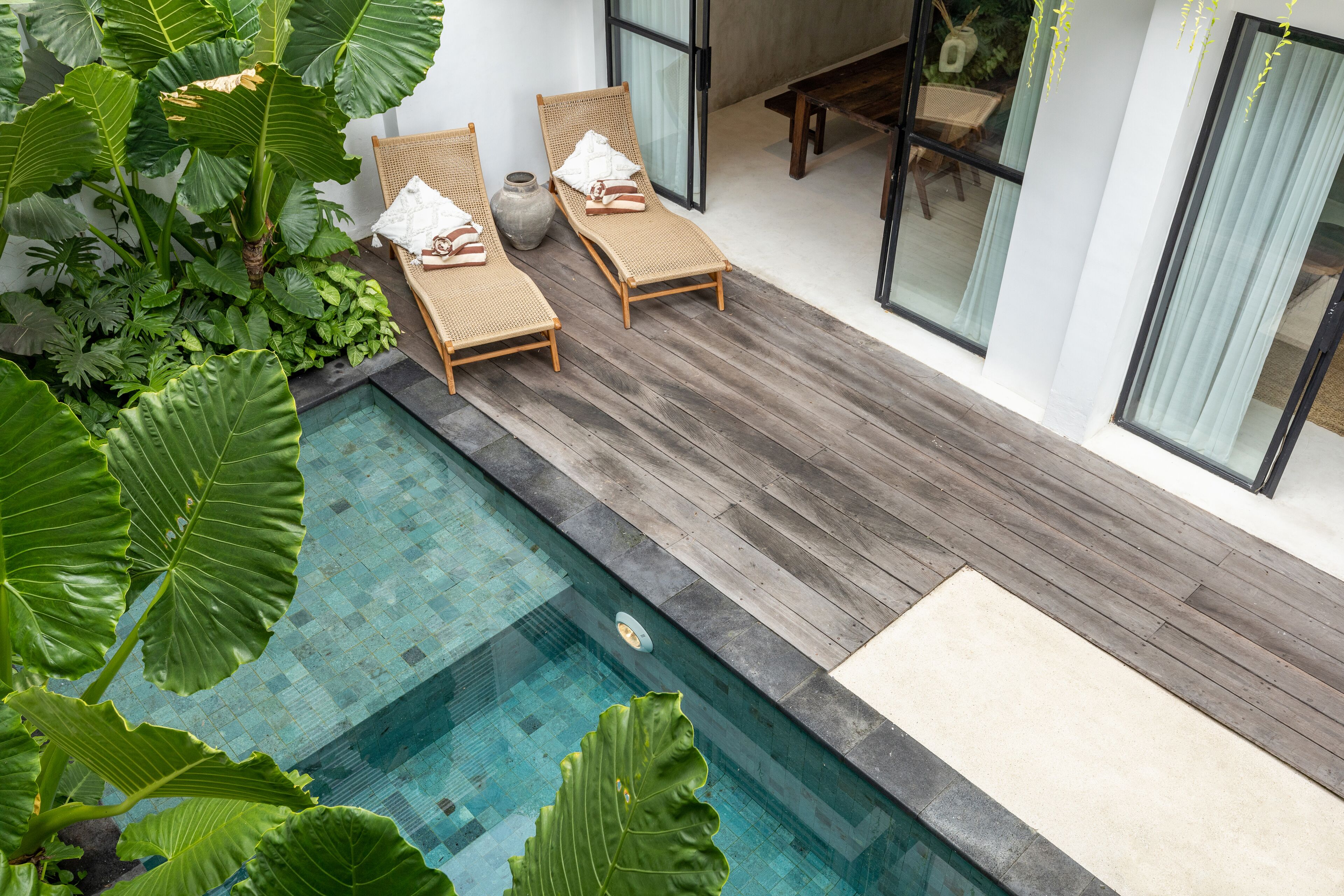 Un espace aménagé au bord de la piscine, comprenant deux chaises longues, une terrasse en bois et une grande plante.