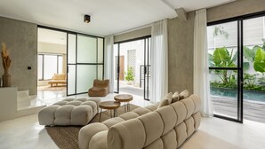 Un salon moderne avec un canapé d’angle, une table basse et un fauteuil en osier. Une grande porte-fenêtre coulissante donne accès à un balcon agrémenté de plantes.