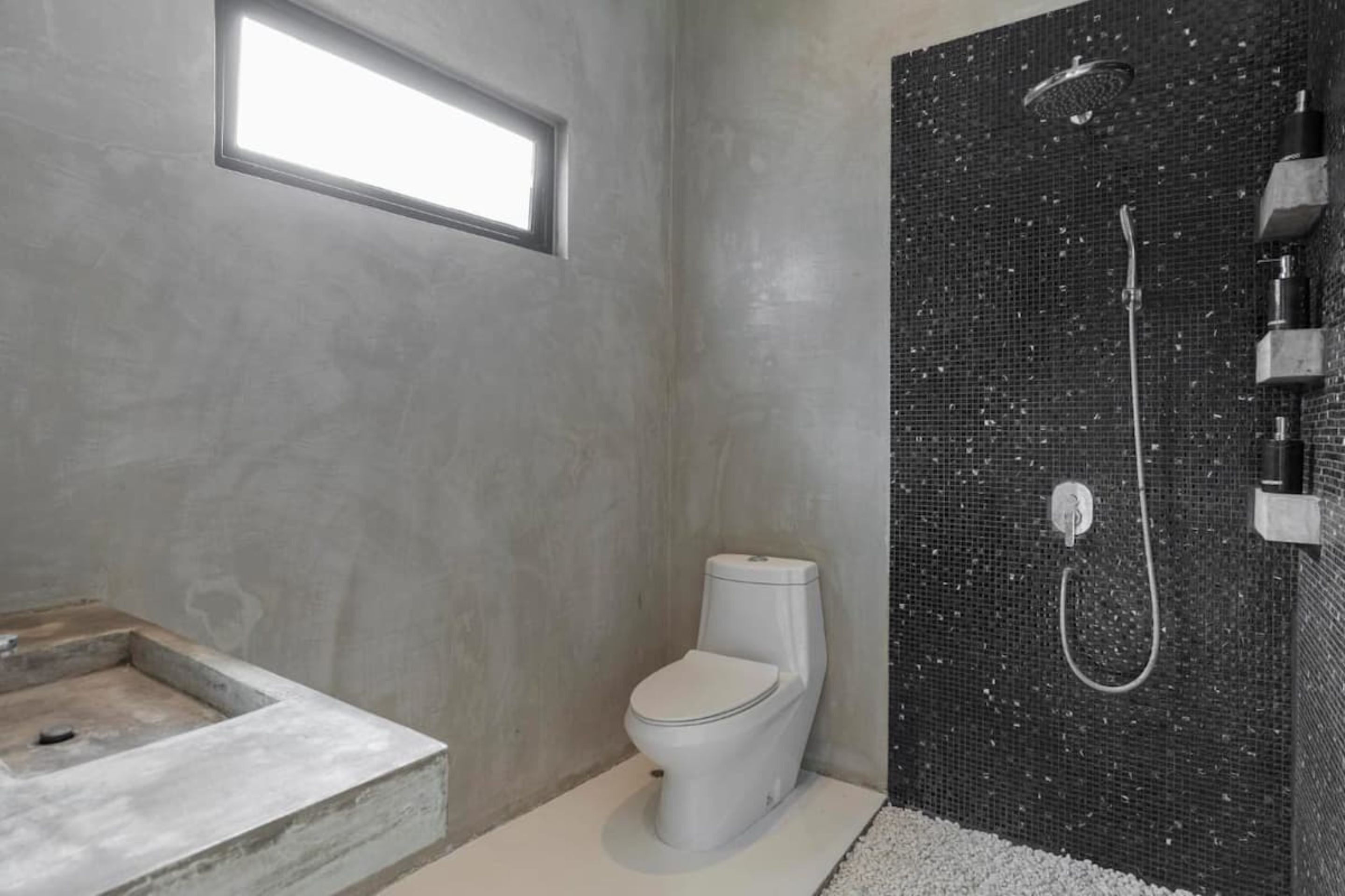 A modern bathroom with a concrete sink, a toilet, and a shower with a mosaic wall.