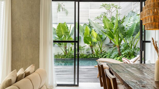 Un salon moderne doté d’une grande porte-fenêtre coulissante qui donne sur un jardin intérieur luxuriant.