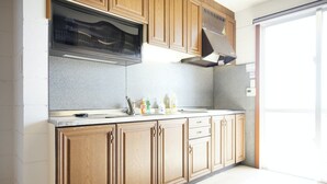 A kitchen with wooden cabinets, a stainless steel range hood, and a window providing natural light. - ITOMAN SEA Pension Odo  MIM (Itoman)