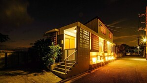 A two-story building with a staircase leading to the entrance, a small garden area, and a street view. - ITOMAN SEA Pension Odo  MIM (Itoman)