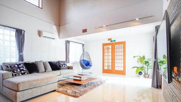A modern living room with a sofa, a glass coffee table, and a hanging chair. There is a wooden door and a TV mounted on the wall. - ITOMAN SEA Pension Odo  MIM (Itoman)