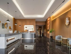 A modern hotel lobby with a reception desk, pendant lighting, and a polished marble floor. - Chonpines Hotel (Yancheng)