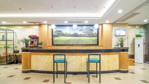 Zona de recepción con mostrador de madera, dos taburetes de bar, una pantalla de televisión grande y una vitrina de vidrio con objetos.