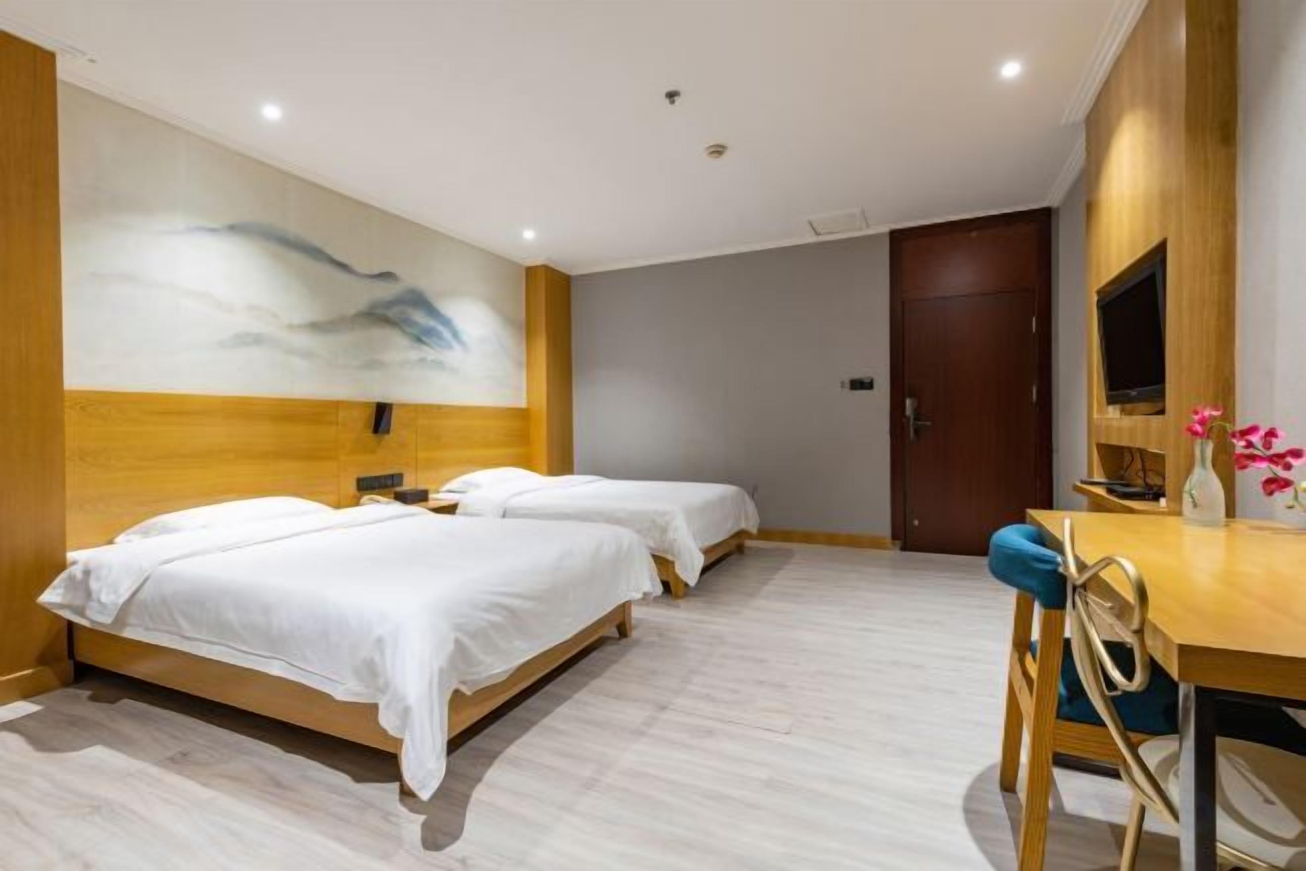 Une chambre d’hôtel avec deux lits, une tête de lit en bois, un bureau avec une chaise et un téléviseur.