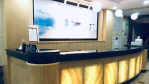 Un mostrador de recepción con una pantalla grande mostrando arte abstracto, un certificado enmarcado y una máquina de café.