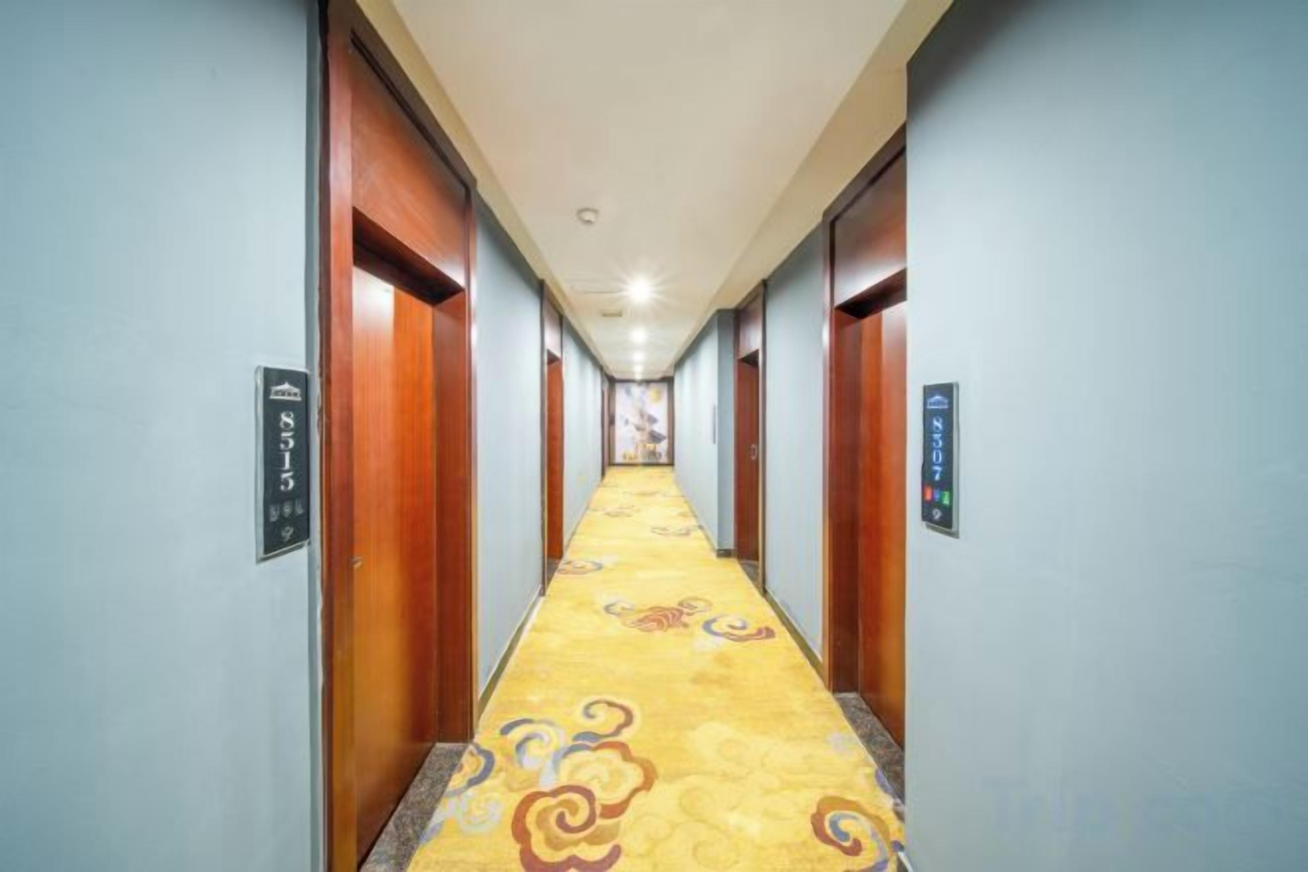 A hotel hallway with carpeted floors, wooden doors, and a light blue wall.