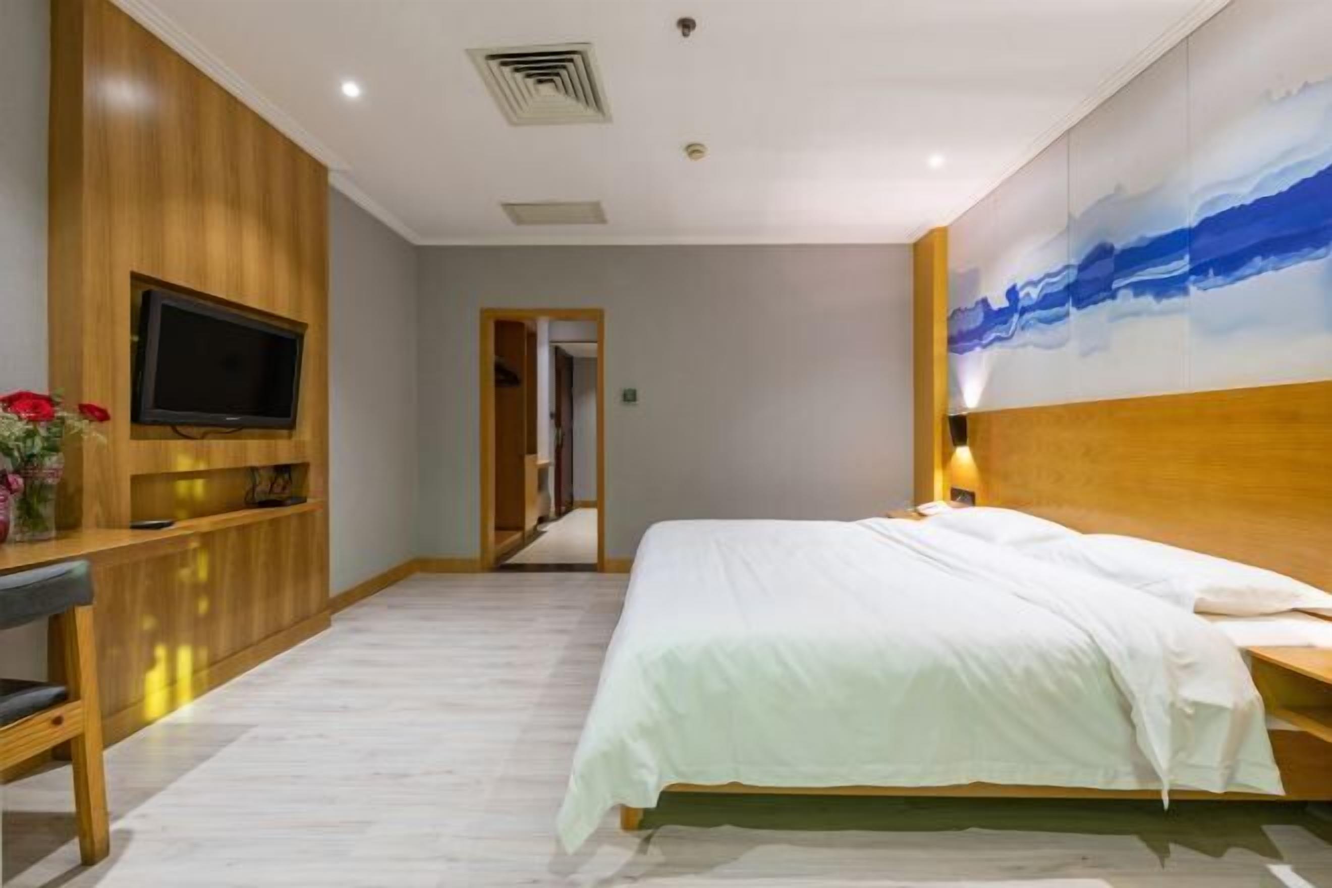 Ein Hotelzimmer mit einem großen Bett, einem an einer Holzwand montierten Fernseher, einem Schreibtisch mit Stuhl und einem Bild an der Wand.