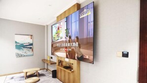 Habitación de hotel con un televisor de pantalla plana grande montado en la pared, una consola de madera, un banco y una alfombra estampada.