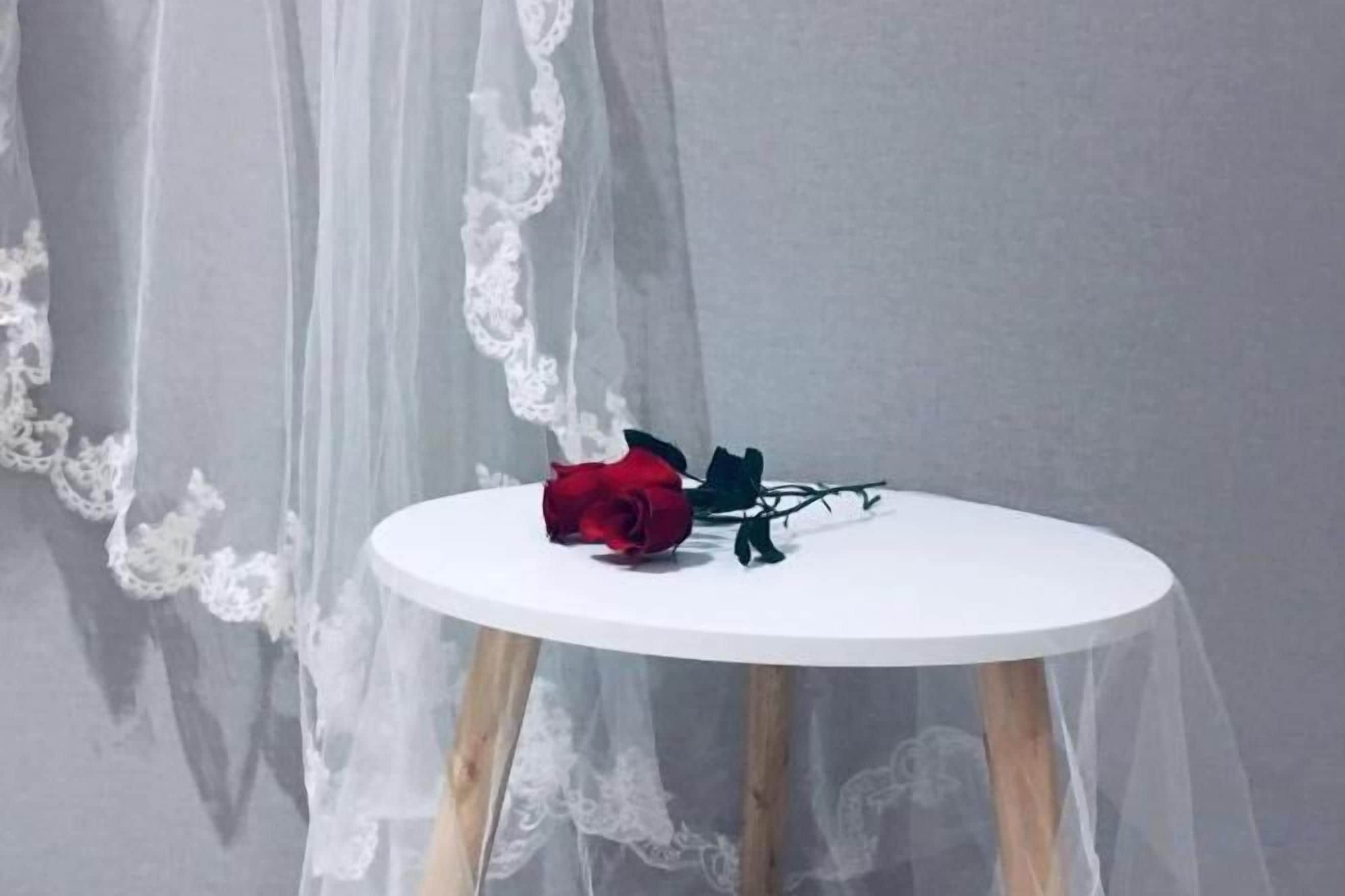 A round table with a white surface and wooden legs, placed against a grey wall with a sheer white lace drape.
