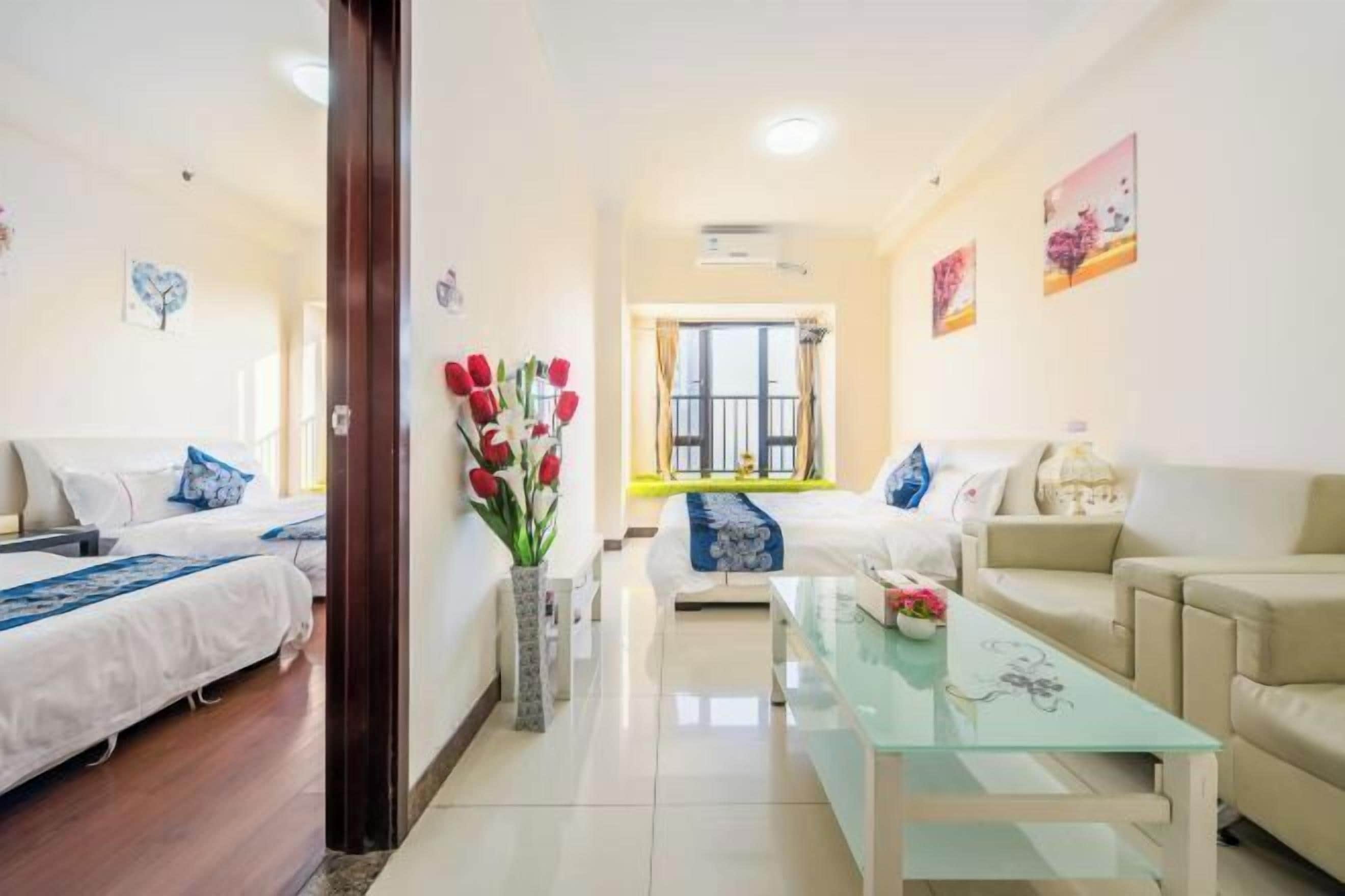Habitación de hotel con dos camas, un sofá, una mesa de centro de cristal y un jarrón con flores.