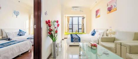 Habitación de hotel con dos camas, un sofá, una mesa de centro de cristal y un jarrón con flores.