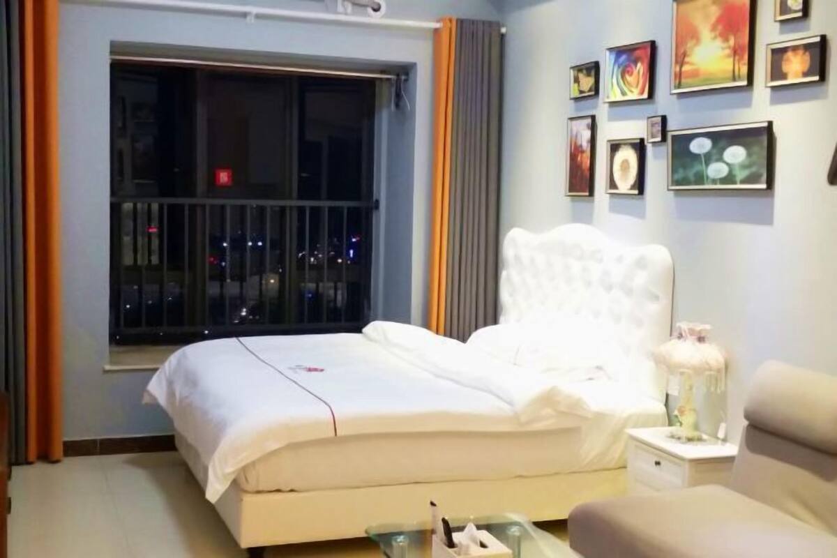 Una habitación de hotel con cama, mesita de noche, cortinas y decoración en la pared.