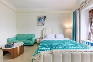 A hotel room with a bed, a teal armchair, a round coffee table, and a painting on the wall. - Huaji Apartment Hostel (Pazhou Complex) (Guangzhou)