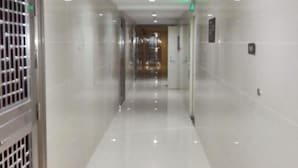 A clean, well-lit hallway with a shiny floor, a metal gate on the left, and a door with a green exit sign on the right. - Huaji Apartment Hostel (Pazhou Complex) (Guangzhou)