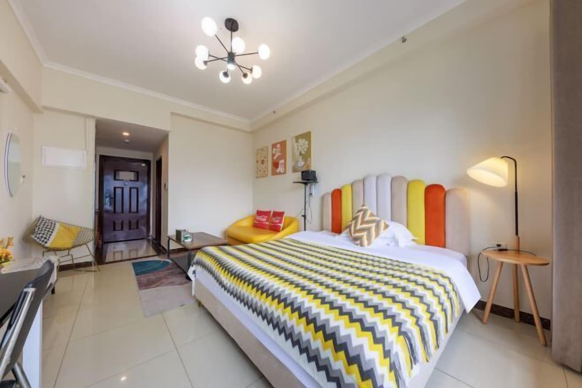 Una habitación de hotel moderna con una cama grande, un escritorio, una silla, una lámpara y una puerta.