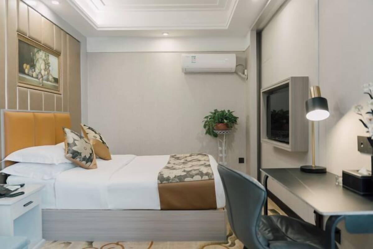 Een hotelkamer met een bed, nachtkastje, televisie, bureau, stoel en een kamerplant.