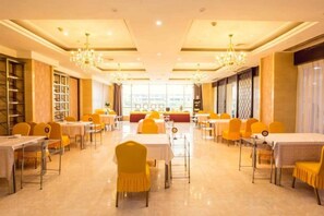 Une salle de banquet avec des tables et des chaises, des lustres et une vue sur l’extérieur grâce à de grandes fenêtres.