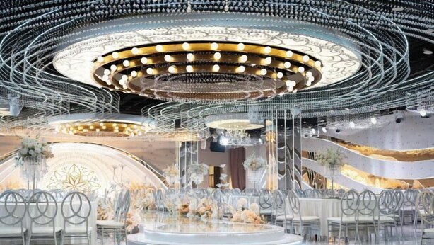 Un interior moderno con un escenario circular, sillas transparentes y centros de mesa florales.