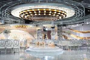 Un interior moderno con un escenario circular, sillas transparentes y centros de mesa florales.