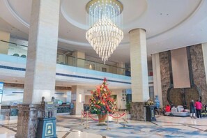 Eine Lobby mit einem großen Kronleuchter, Marmorsäulen, einem Empfangstisch und einer dekorativen Blumenkomposition.