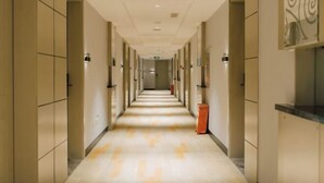Un pasillo de hotel con una distribución larga y estrecha, múltiples puertas y suelo alfombrado.