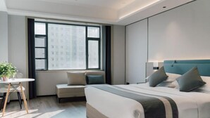 Una habitación de hotel moderna con una cama grande, un sofá, una mesita con una planta y una ventana con vistas a la ciudad.