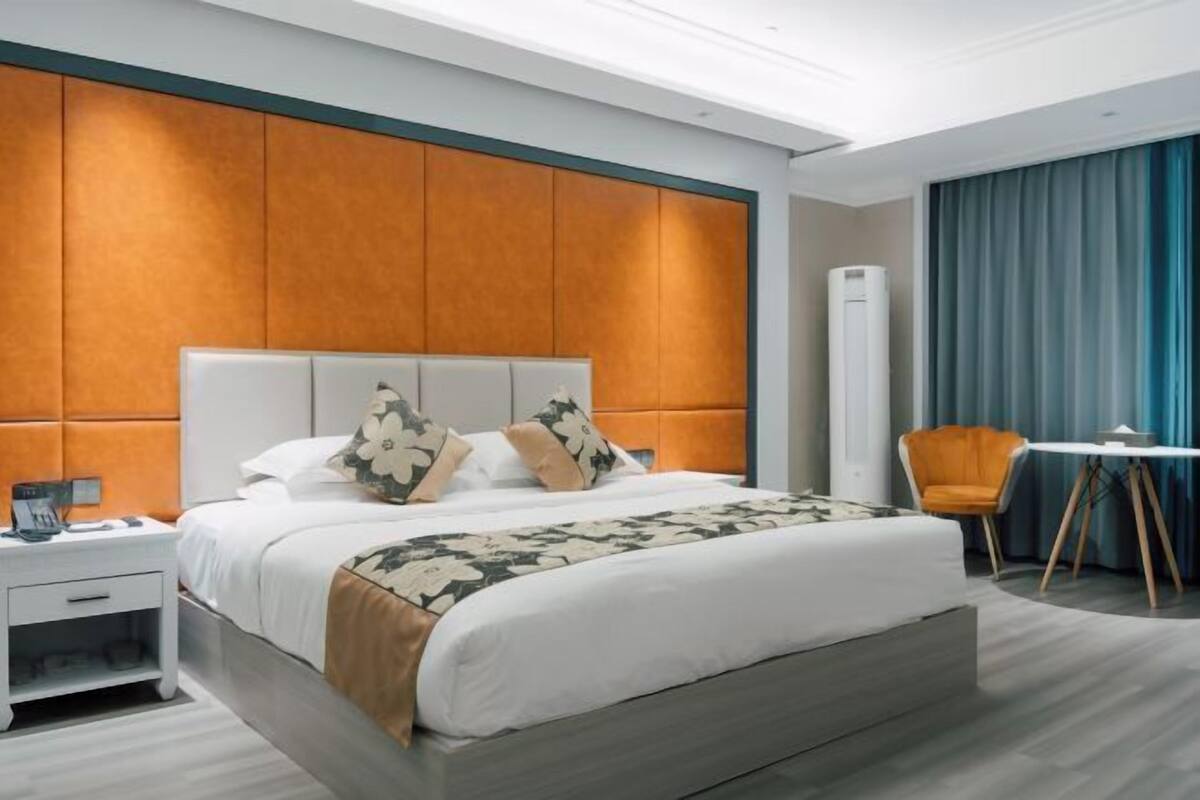 Een moderne hotelkamer met een groot bed, een nachtkastje, een stoel, een tafeltje en een raam met gordijnen.