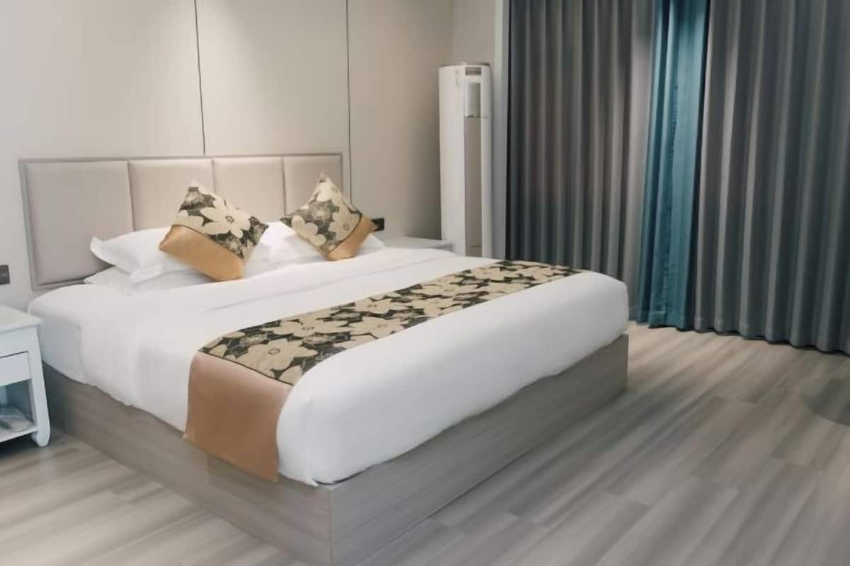 Een moderne hotelkamer met een groot bed, nachtkastje, een wandairconditioner en een raam met gordijnen.