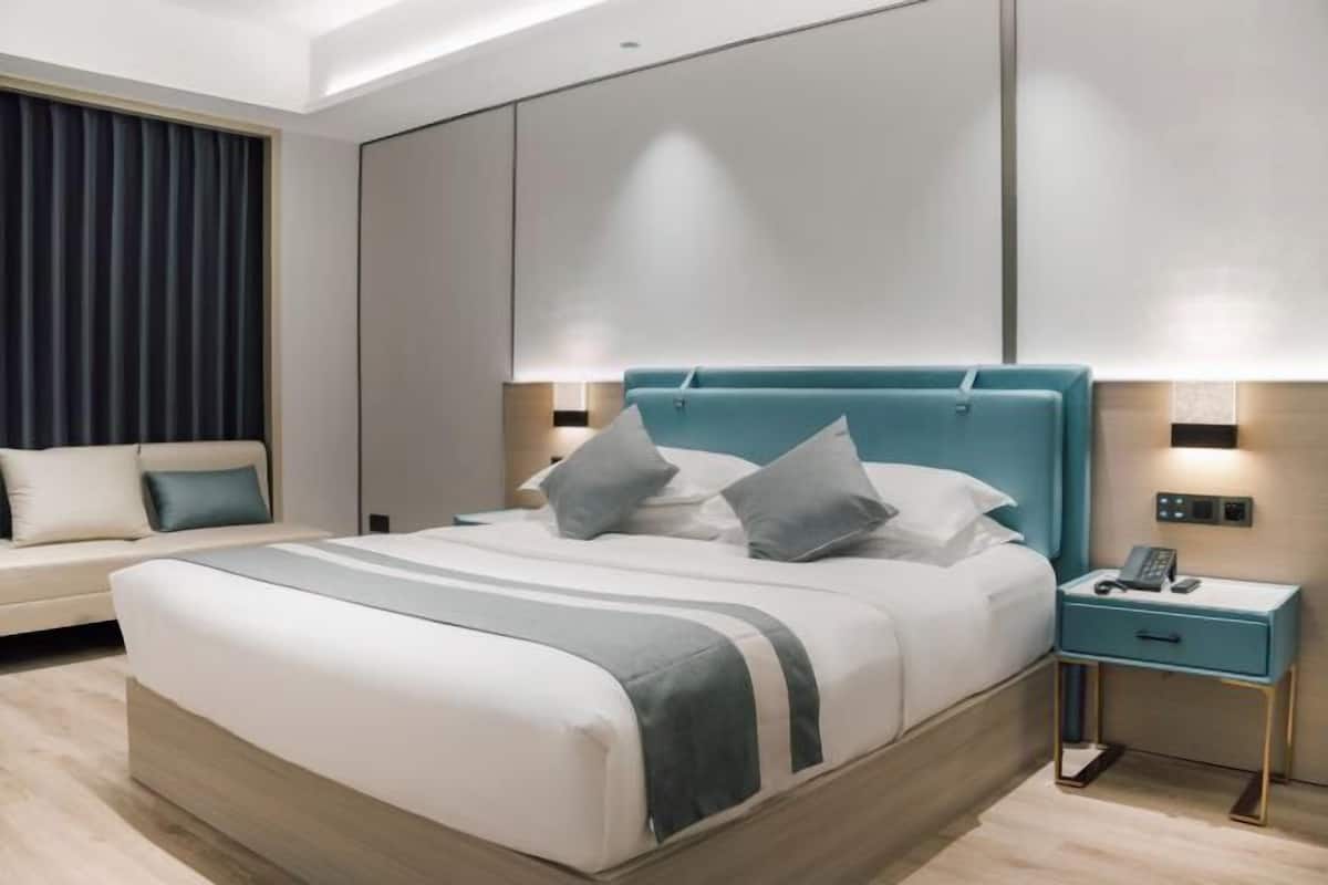 Een moderne hotelkamer met een groot bed, een nachtkastje met een telefoon en een bankje in de hoek.