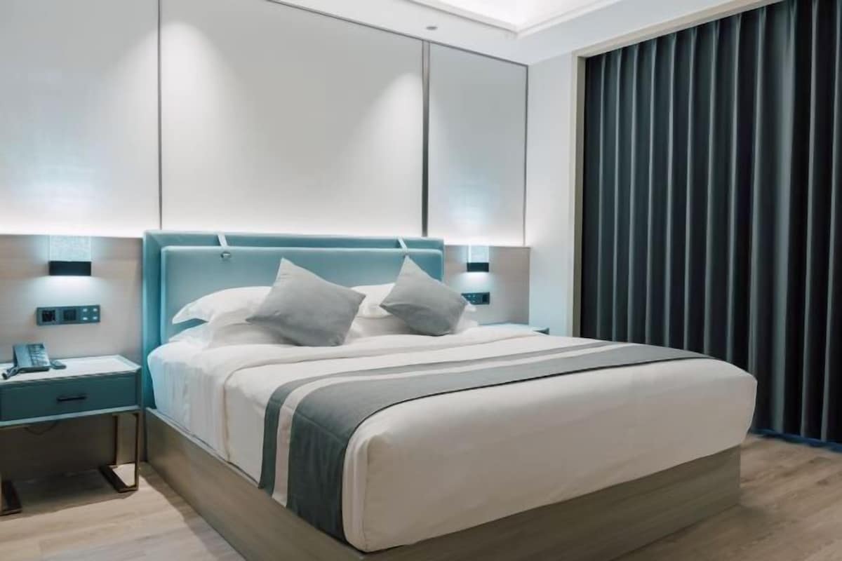 Une chambre moderne avec un grand lit, une table de chevet, une commode et un panneau de commande fixé au mur.