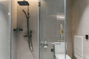Une salle de bain moderne dotée d’une douche à parois de verre, d’un pommeau de douche à main et de toilettes équipées d’une barre d’appui.