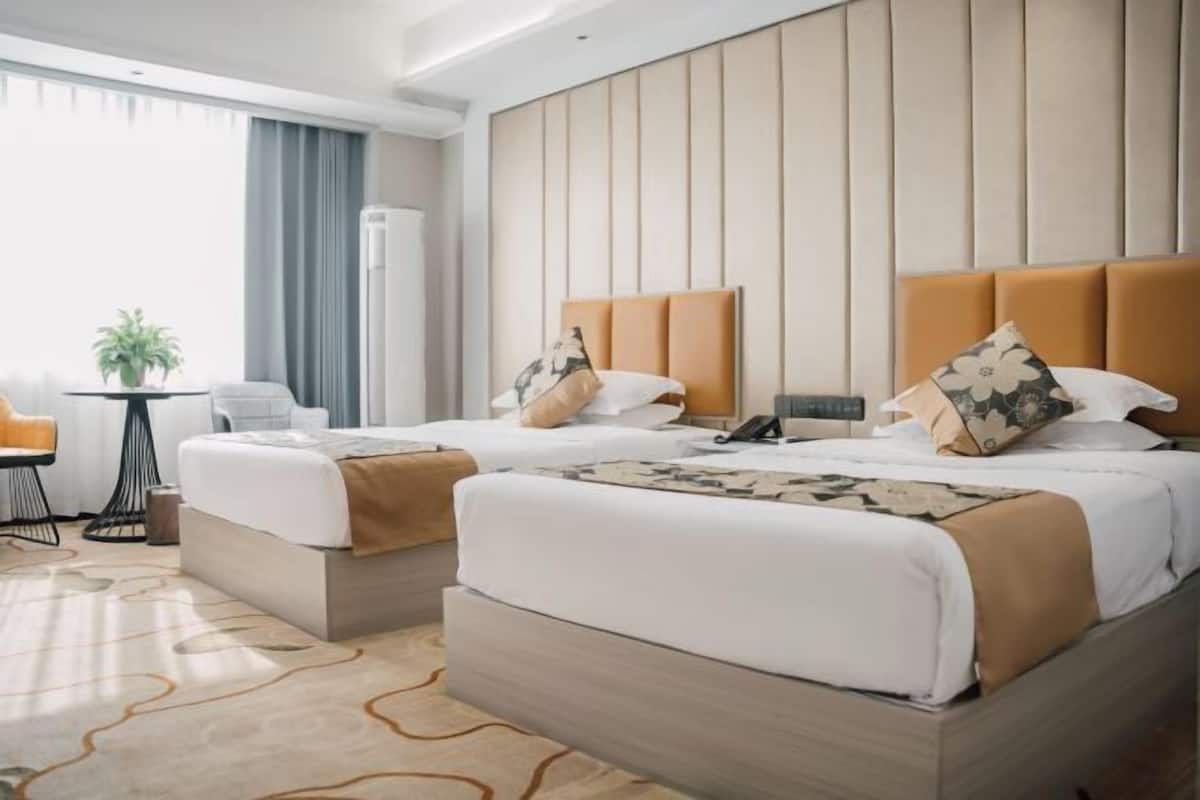 Hotelkamer met twee bedden, een bureau, een stoel, een plant en een groot raam.